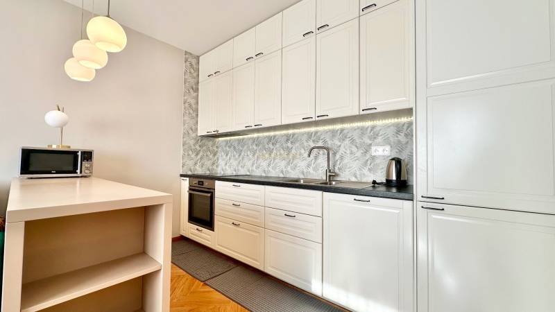 Küche in einer 3-Zimmer-Wohnung mit weißen Schränken und einem Boden in Holzoptik.