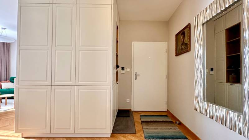 Eingangsbereich mit weißem Schrank, Spiegel, Bild und Boden mit Holzdekor in einer 3-Zimmer-Wohnung.