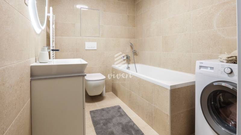 Badezimmer in einer Einzimmerwohnung mit Badewanne, Waschmaschine und Toilette in neutralen Tönen.