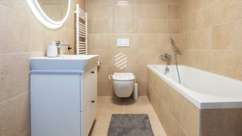Ein beige gehaltenes Badezimmer mit Badewanne, Waschbecken und Spiegel in einer Einzimmerwohnung.