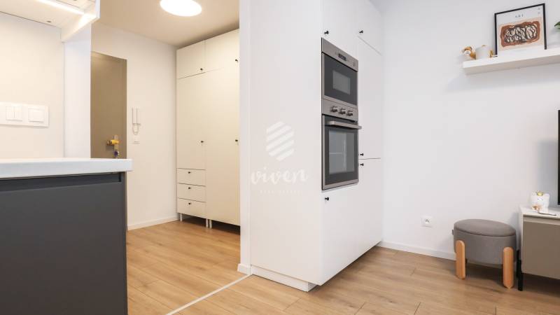 Küche in einer Einzimmerwohnung mit weißen Schränken und einem Boden in Holzoptik.