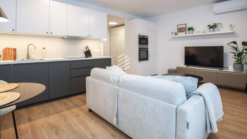 Wohnzimmer einer Einzimmerwohnung mit Küchenzeile, Sofa und Boden in Holzoptik.