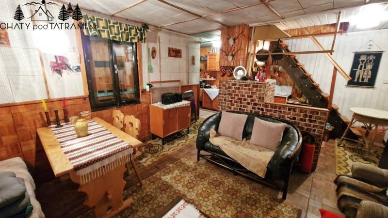 Innenraum einer Hütte mit Sofa, Holzboden, Esstisch und Treppe.