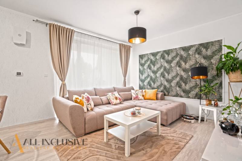 Wohnzimmer mit beigem Sofa, weißem Tisch und Tapete mit Naturmotiv.