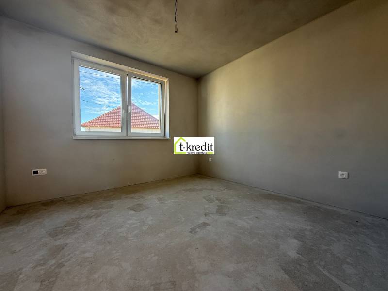 Izba v rodinnom dome, steny bez dekorácií, vidno strechu susednej budovy.