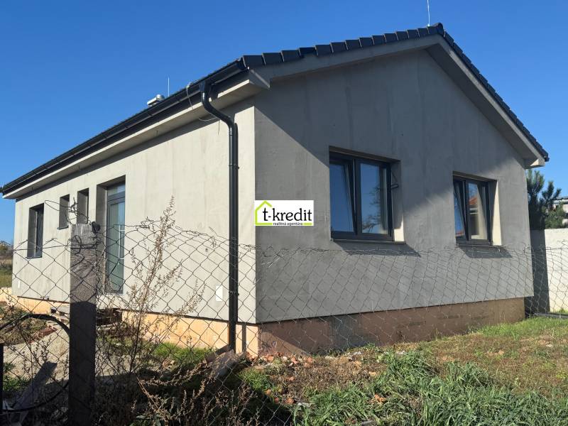 Ein Einfamilienhaus in Tesárske Mlyňany mit grauer Fassade und Fenstern, eingezäunt mit einem Maschendrahtzaun.