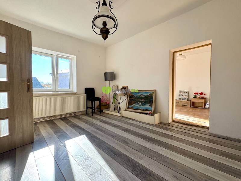 Ein Zimmer in einem Einfamilienhaus mit weißen Wänden, einem Boden in Holzoptik und einem großen Fenster.