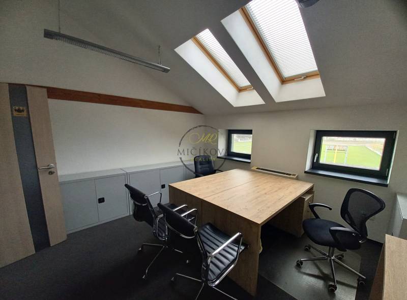 Ein Büro mit einem Schreibtisch und Stühlen, unter Dachfenstern, mit einem Boden in Holzoptik.