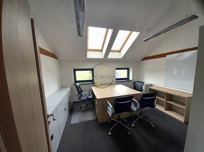 Ein Büro mit einem Boden in Holzoptik, Dachfenstern und Tischen mit Stühlen.