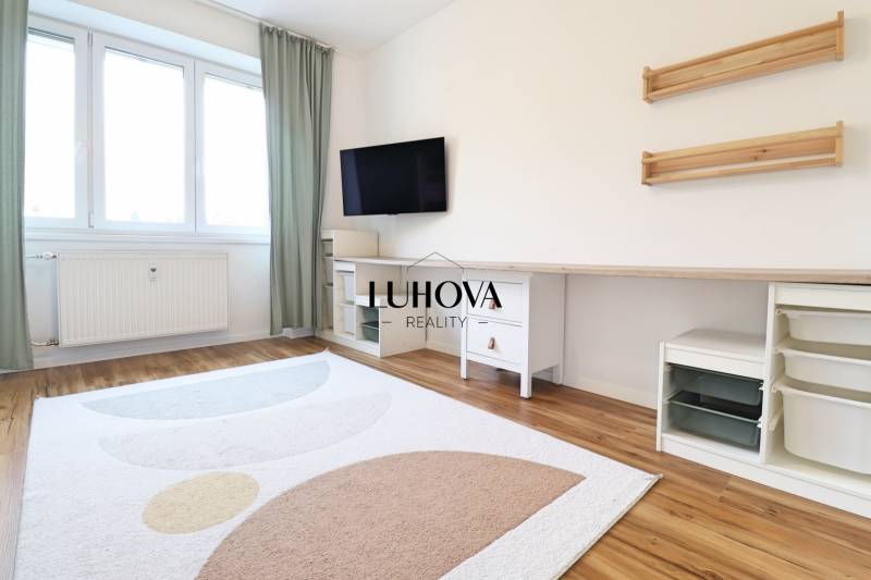 Ein Zimmer in einer 3-Zimmer-Wohnung mit Fernseher, weißen Möbeln und einem Boden in Holzoptik.