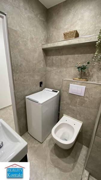 Badezimmer in einer Einzimmerwohnung mit Waschmaschine und Toilette, ergänzt durch ein Ablageregal.