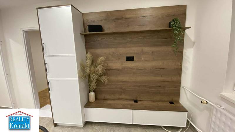 In der 1-Zimmer-Wohnung gibt es eine Schrankwand mit Holzdekor und Blumen in einer Vase.