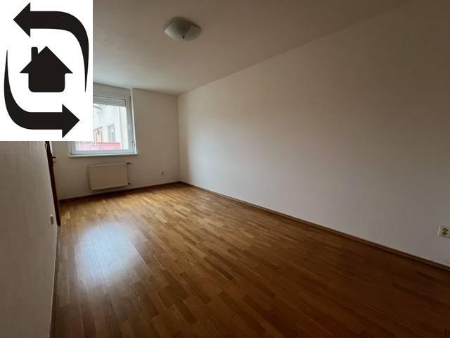 Ein leerer Raum in einer 3-Zimmer-Wohnung mit Holzboden und Fenster.