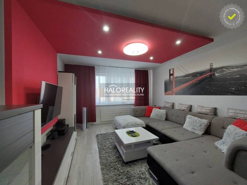 Wohnzimmer in einer 3-Zimmer-Wohnung mit Sofa, Fernseher und roten Dekorationen.