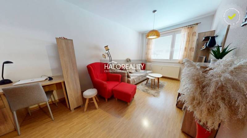 Wohnzimmer in einer Zweizimmerwohnung mit einem Tisch, einem roten Sessel und einem Boden in Holzoptik.