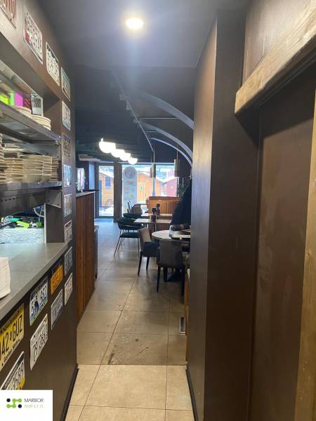 Innenraum von Gastronomiebereichen mit Tellern auf einem Regal, Tafeln, Tischen und Stühlen.