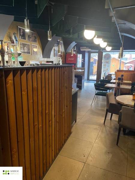 Innenraum von Gastronomiebereichen mit einer Holzbar und Tischen. Auch dekorative Beleuchtung ist zu sehen.