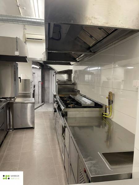 Professionelle Küche mit Edelstahlgeräten und weißen Fliesen in Gastronomieräumen.