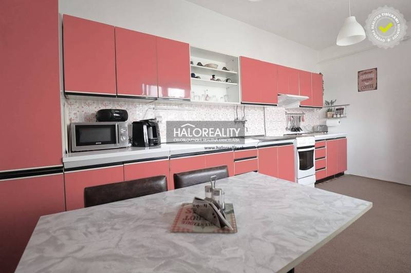 Küche in einem Einfamilienhaus mit rosa Schränken und einem weißen Tisch.