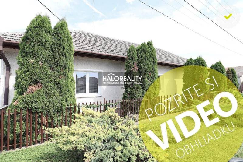 Ein Einfamilienhaus in Veľký Kýr mit einem gepflegten Garten, grünen Thujen und einem Zaun.