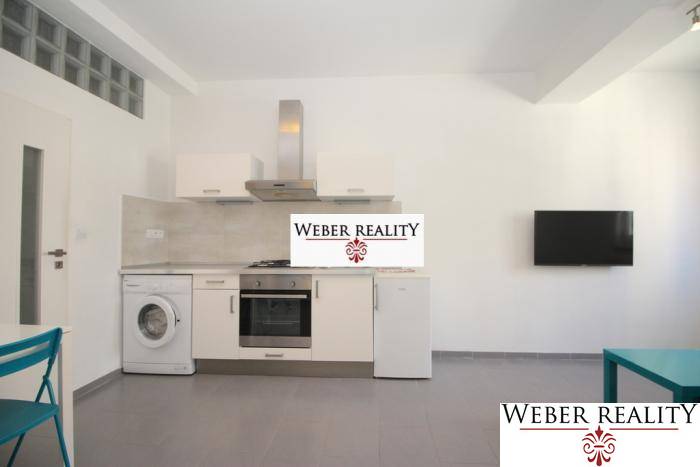 Küche in einer 2-Zimmer-Wohnung mit weißer Küchenzeile, Waschmaschine und Fernseher an der Wand.