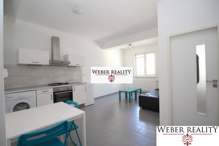 Wohnzimmer in einer 2-Zimmer-Wohnung mit Küchenzeile, einfacher Einrichtung und Fenster.