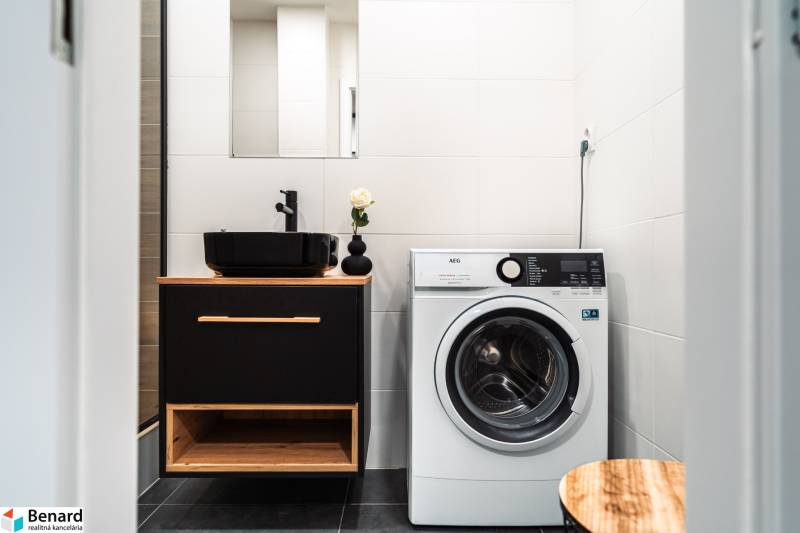 Badezimmer in einer 2-Zimmer-Wohnung mit Waschbecken, Waschmaschine und schwarzen Accessoires.