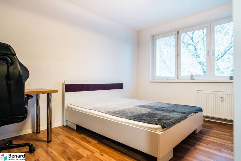 Schlafzimmer mit Bett, Tisch und Boden in Holzdekor in einer 2-Zimmer-Wohnung.
