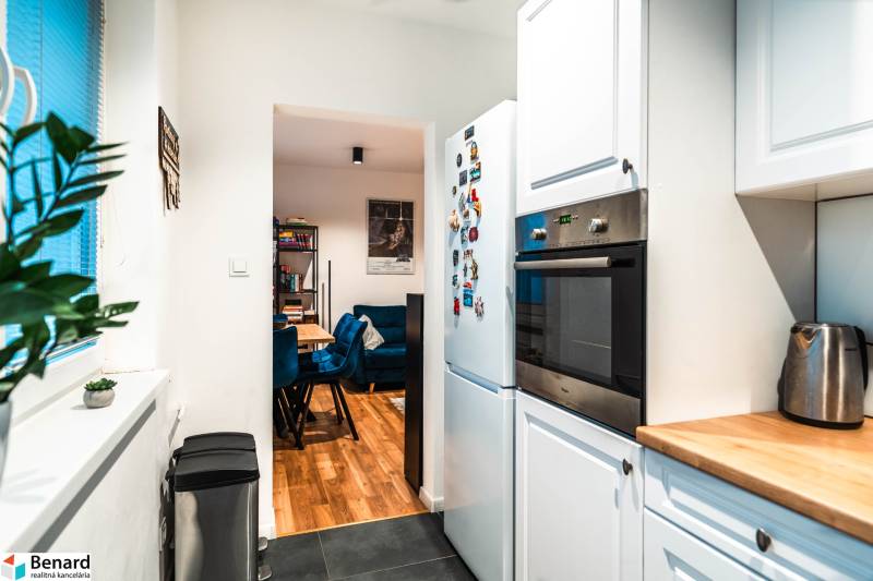 Die Küche einer Zweizimmerwohnung mit weißen Schränken, Geräten und Blick ins Esszimmer.