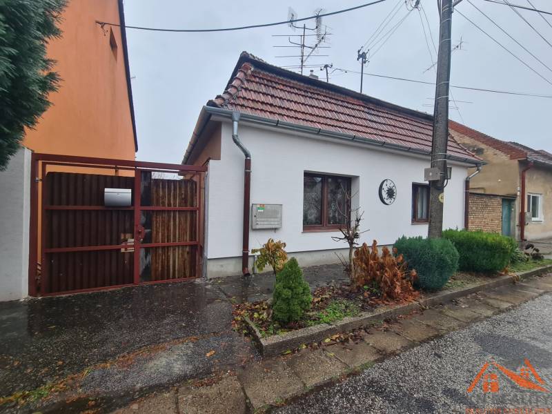 Ein Einfamilienhaus in Komárno mit einem Satteldach und einem Eingangstor, Vorgarten mit Sträuchern.