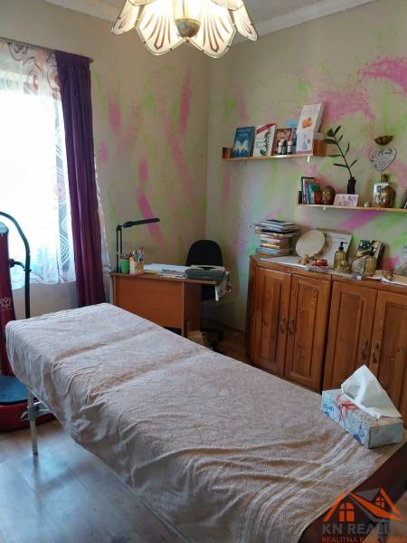 Ein Zimmer in einem Einfamilienhaus mit einem Massagetisch, einem Schreibtisch und Bücherregalen.