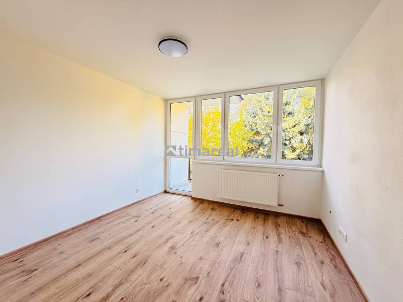 Ein Zimmer mit großen Fenstern und einem Boden in Holzoptik in einer 3-Zimmer-Wohnung.