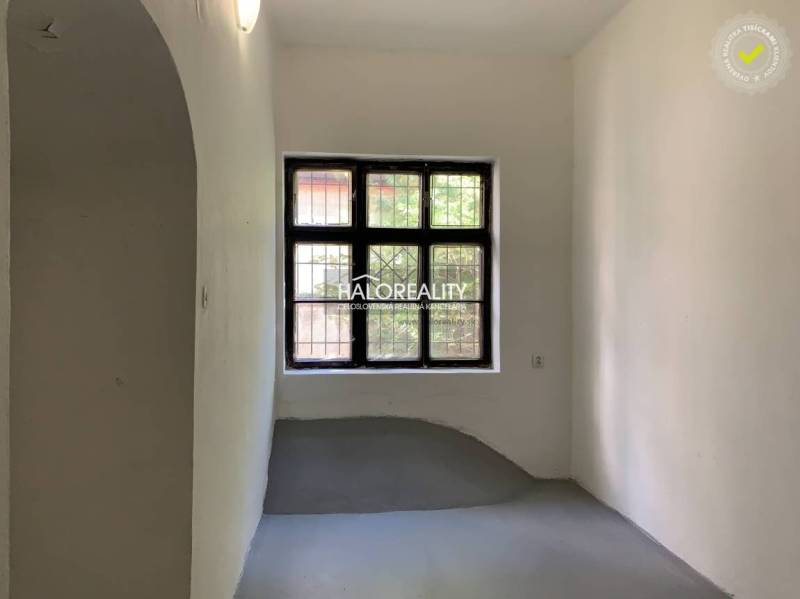 Ein schmaler Raum mit weißen Wänden, ein Fenster mit Gitter, ein grauer Boden im Büro.