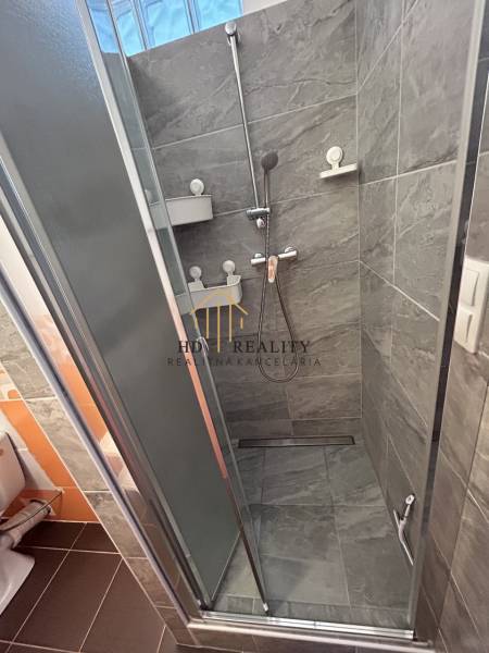 Badezimmer mit dunklen Fliesen und Duschkabine in einer Einzimmerwohnung.