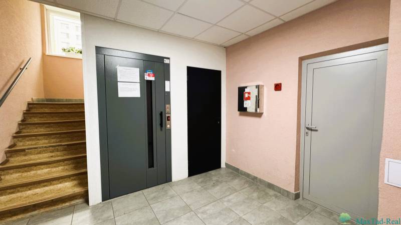 Ein Flur mit Treppen, Aufzug, Fliesen und Feuerlöscher in einer 3-Zimmer-Wohnung.