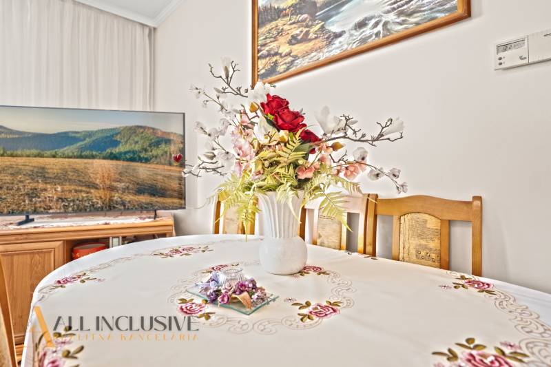 Esszimmer in einem Einfamilienhaus mit Blumendekoration auf dem Tisch und einem Fernseher im Hintergrund.