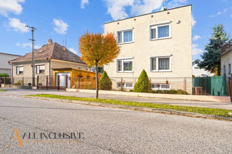 Einfamilienhäuser in Dunajská Streda, von Bäumen gesäumte Straßen, Gitterzäune, blauer Himmel.