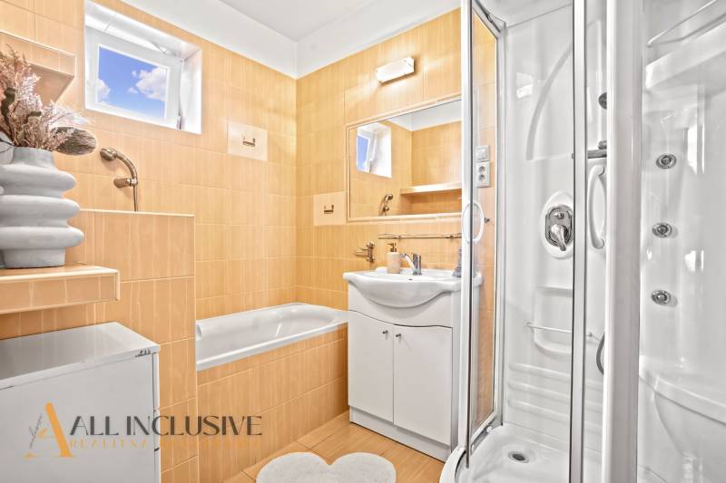 Ein Badezimmer in einem Einfamilienhaus mit einer Badewanne, einer Dusche und einem Spiegel auf ockerfarbenen Fliesen.