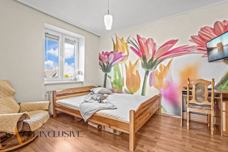 Ein Schlafzimmer in einem Einfamilienhaus mit einer farbenfrohen Blumen-Tapete und einem Boden in Holzoptik.