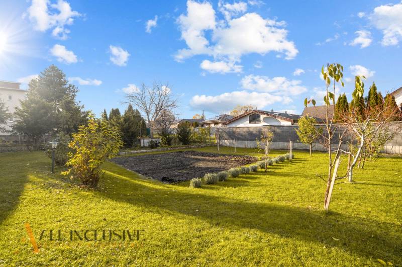 Der Garten eines Einfamilienhauses in Dunajská Streda mit Rasen, Bäumen und einem gepflegten Blumenbeet.