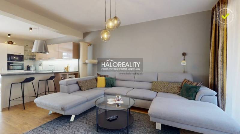 Ein geräumiges Wohnzimmer in einem Einfamilienhaus mit einem Sofa, einer Küchenzeile und einem Boden in Holzoptik.