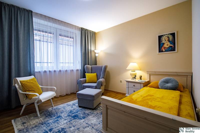 Ein Zimmer in einem Einfamilienhaus mit einem Bett, einem Sessel, einem Tisch und einem Boden in Holzoptik.