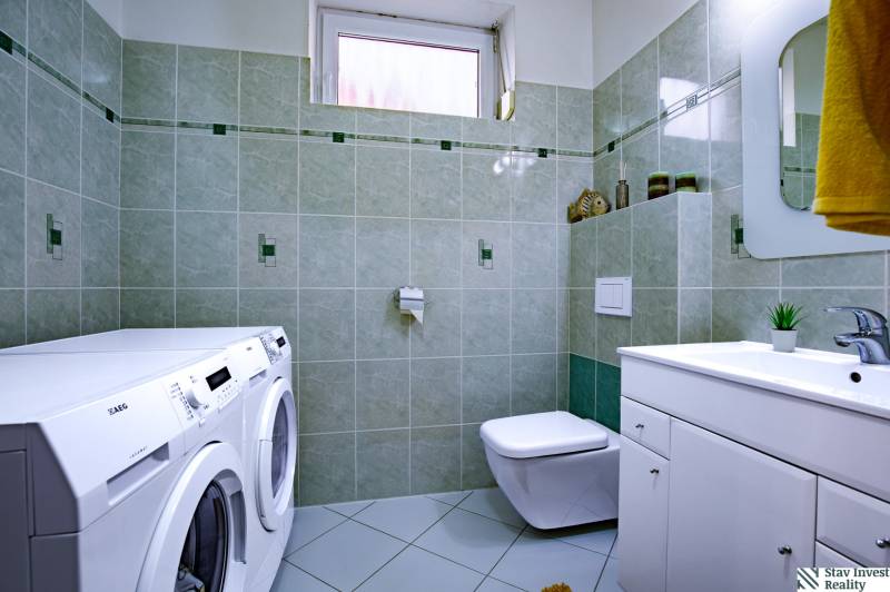 Badezimmer im Einfamilienhaus mit Waschmaschine, Trockner, Waschbecken und Toilette, grüne Fliesen.