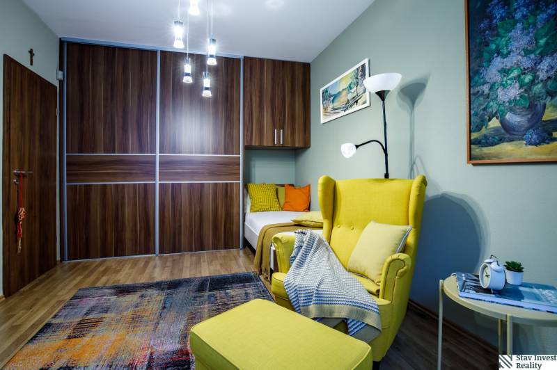 Ein Zimmer mit einem bequemen Sessel, einem Kleiderschrank, einem Kronleuchter und einem Boden mit Holzdekor in einem Einfamilienhaus.