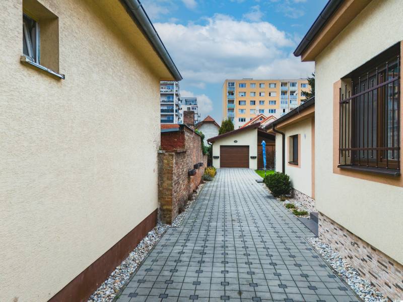 Blick auf den Hof eines Einfamilienhauses von der Školská-Straße in Senec mit Gehweg und Sträuchern.