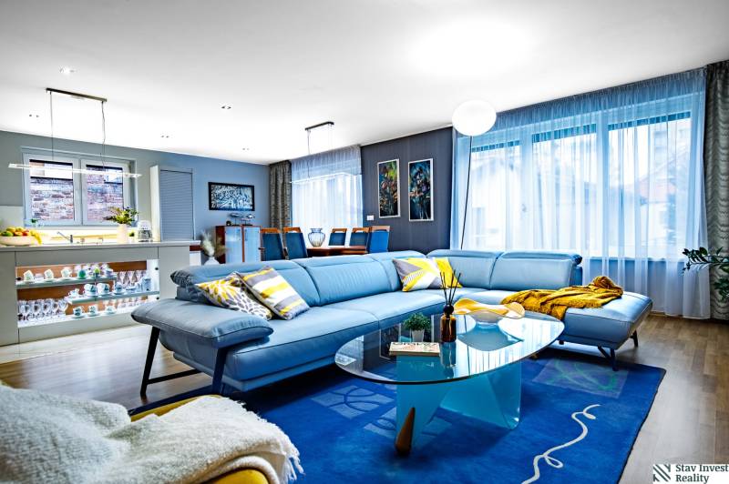 Wohnzimmer in einem Einfamilienhaus mit einem blauen Sofa, einem Glastisch und einem Boden in Holzoptik.