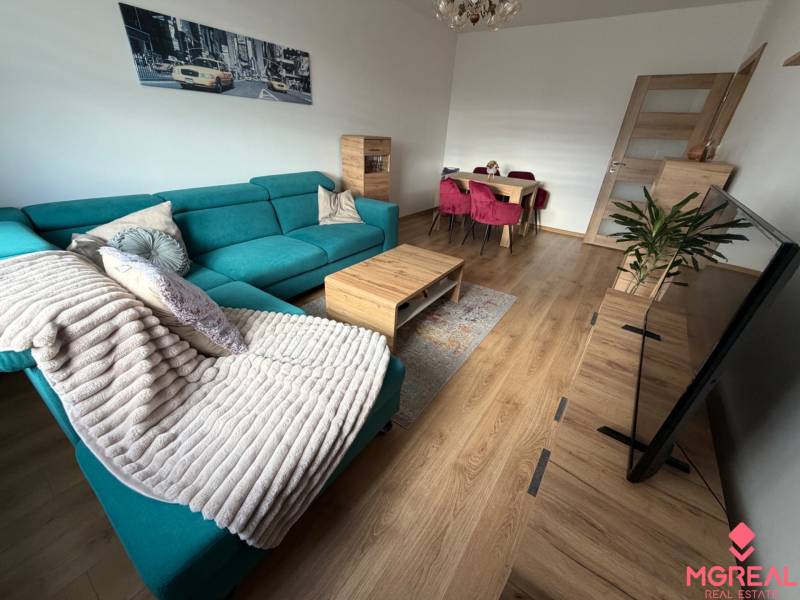 Wohnzimmer einer 4-Zimmer-Wohnung mit einer türkisfarbenen Couch, einem Boden in Holzoptik und einem Esstisch.
