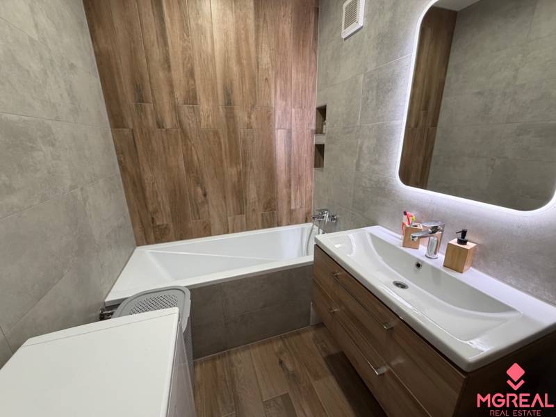 Badezimmer mit Spiegel, Badewanne, Waschbecken und Boden mit Holzdekor in einer 4-Zimmer-Wohnung.