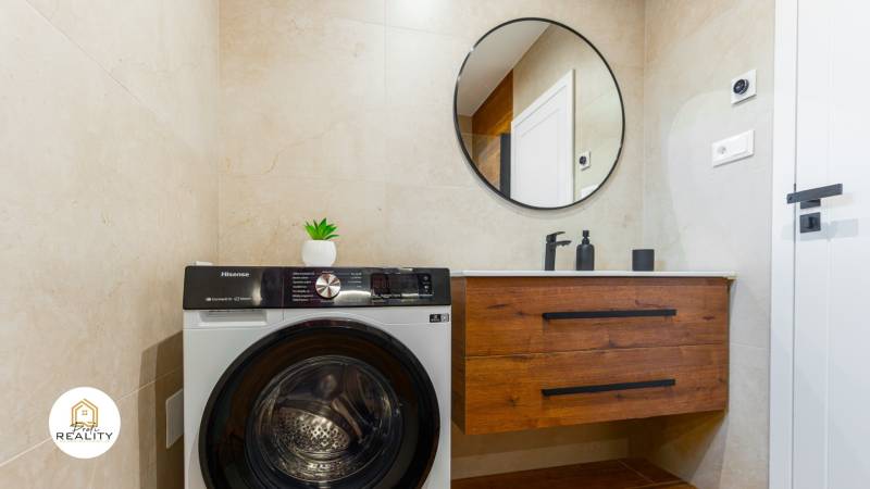 Badezimmer in einer Einzimmerwohnung mit Waschmaschine, rundem Spiegel und Schrank.