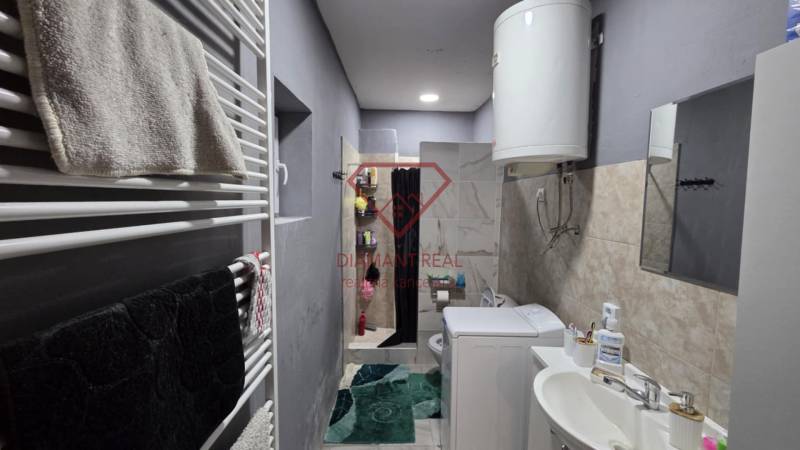 Ein Badezimmer in einem Einfamilienhaus mit Waschbecken, Waschmaschine, Boiler und Duschkabine.